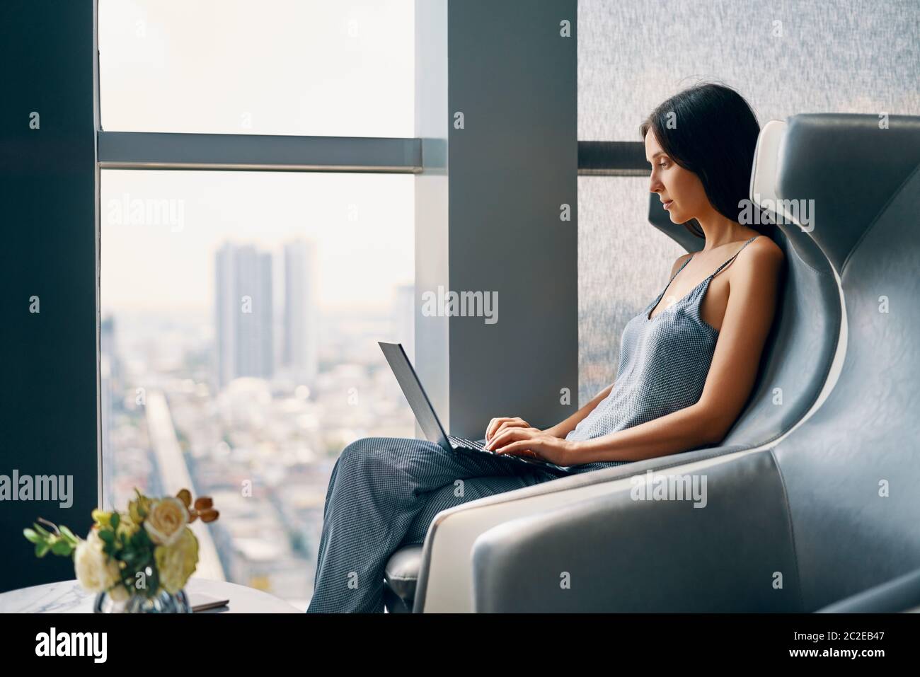 Giovane donna che lavora su un computer portatile mentre si siede in una grande e comoda sedia all'interno moderno Foto Stock