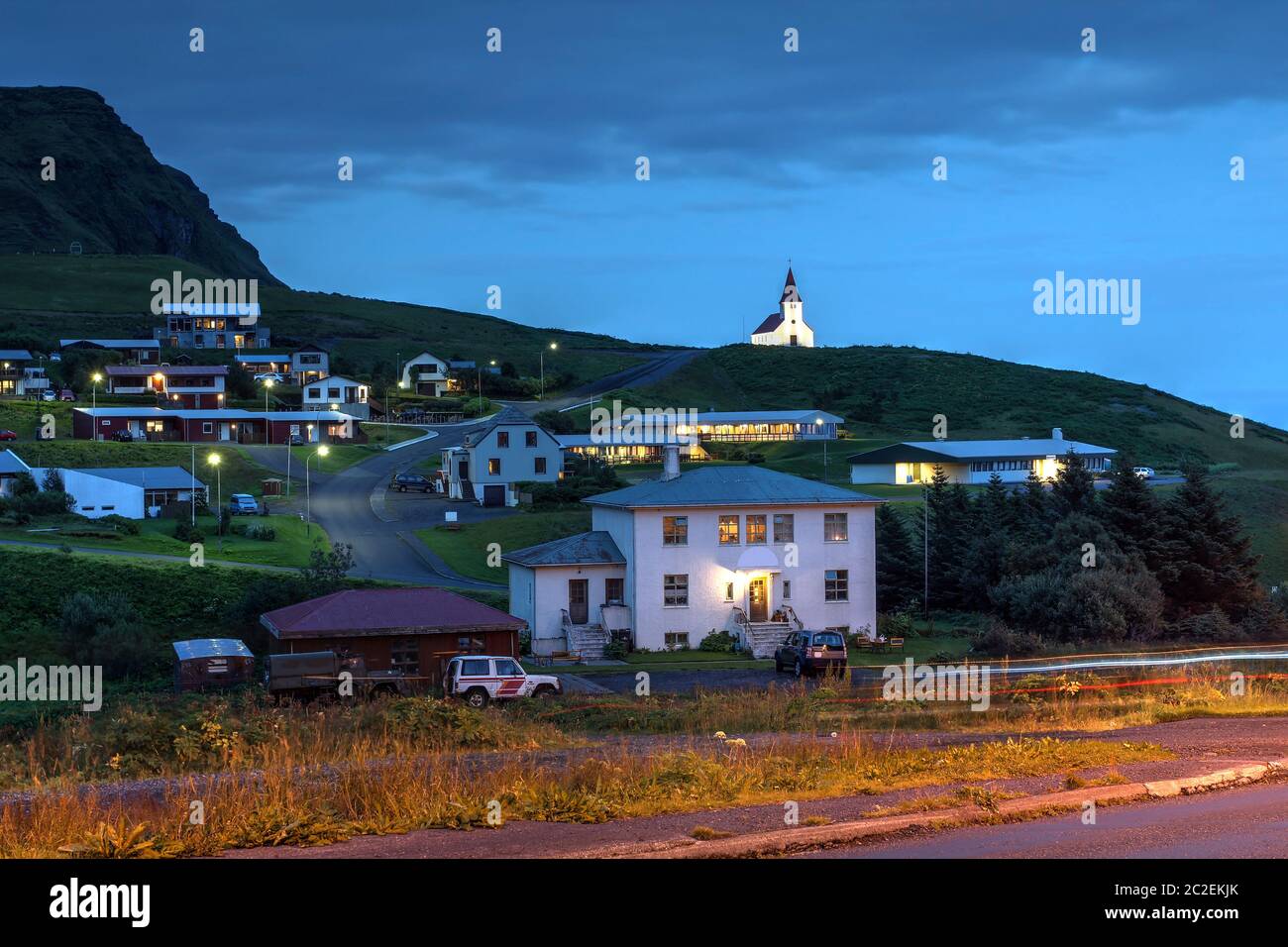 Scena notturna di Vik (Vik i Myrdal), il villaggio più meridionale dell'Islanda con la sua chiesa che si affaccia sulle case sparse e un letto e una festa di rottura. Foto Stock