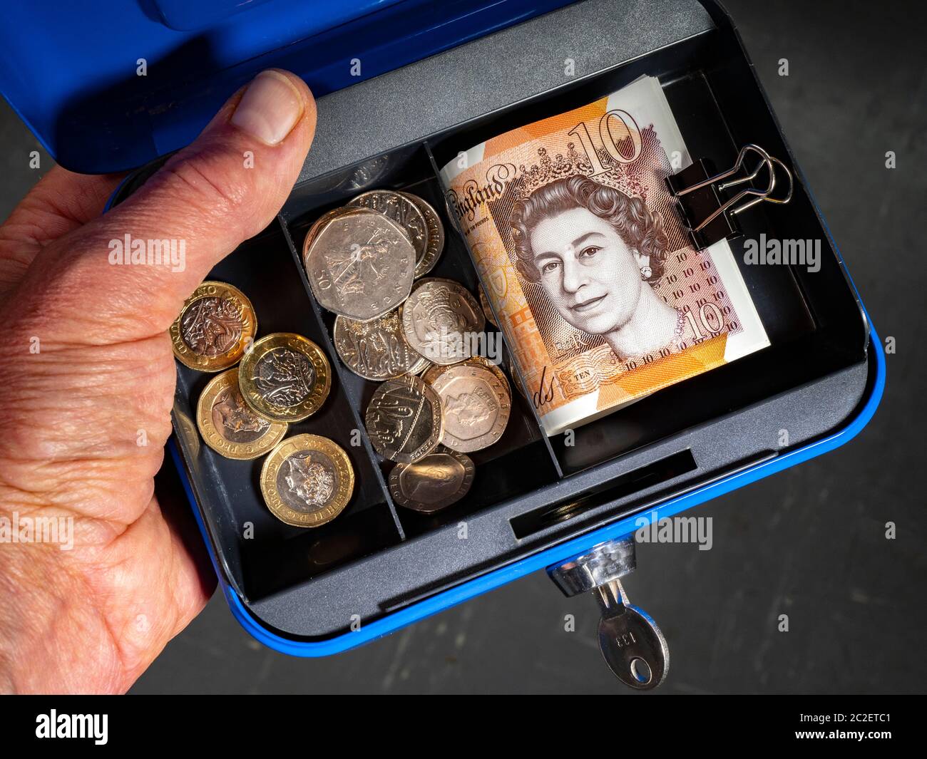 Mano dell'uomo su una piccola cassetta di sicurezza personale, blu, aperta,  con chiave nella serratura, contenente una serie di sterline in contanti,  banconote e monete Foto stock - Alamy