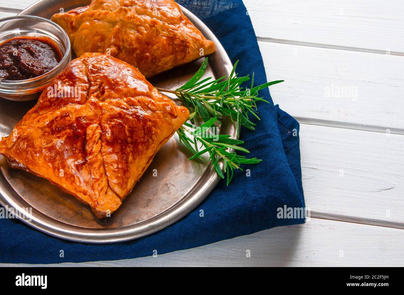 Dolci fatti in casa con carne e salsa piccante con rosmarino serviti su un vassoio di metallo su un tavolo di legno bianco Foto Stock