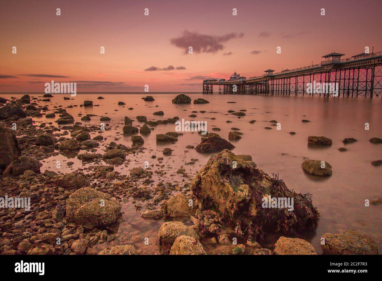 Molo di Llandudno al tramonto con mare liscio e rocce. Destinazione turistica del Galles del Nord per le vacanze Foto Stock