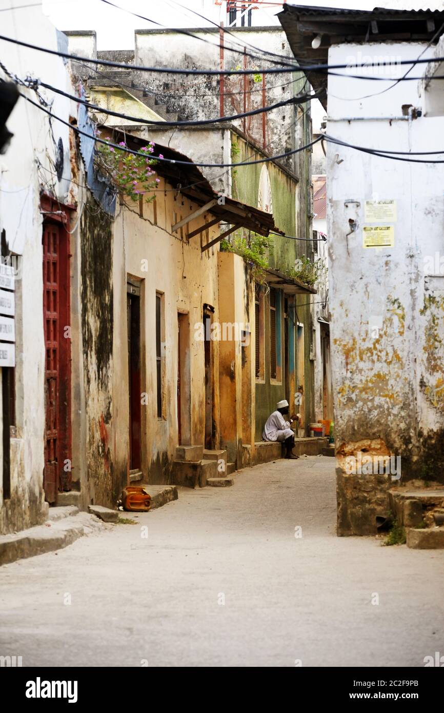 Un uomo si siede alla porta del suo negozio con regali per i turisti a Stone Town Foto Stock