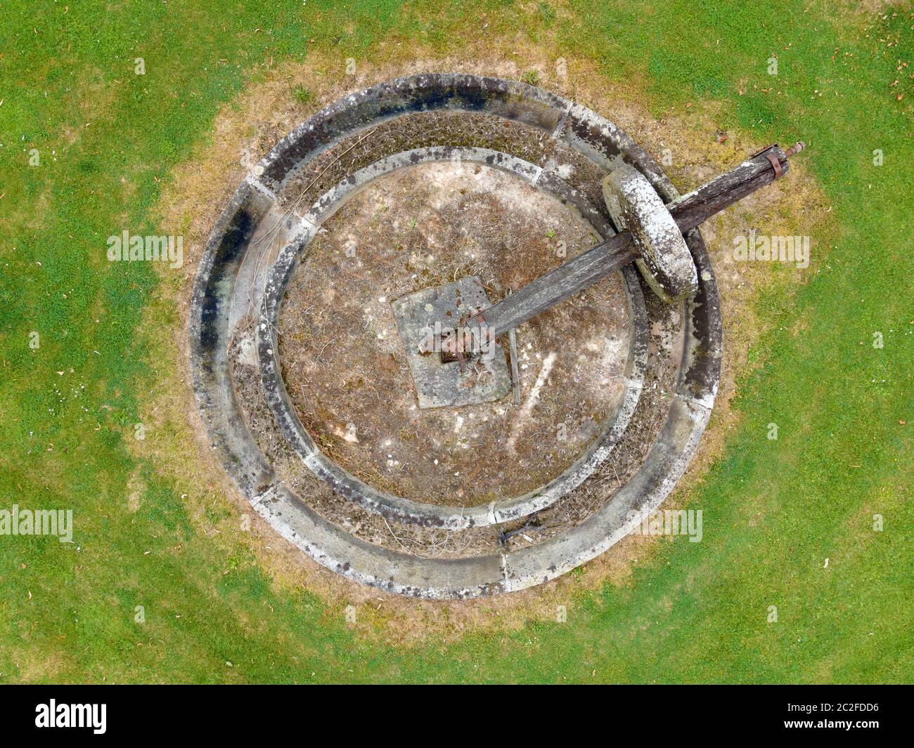 vista aerea di una antica macina circolare con asse di legno su sfondo verde erba Foto Stock