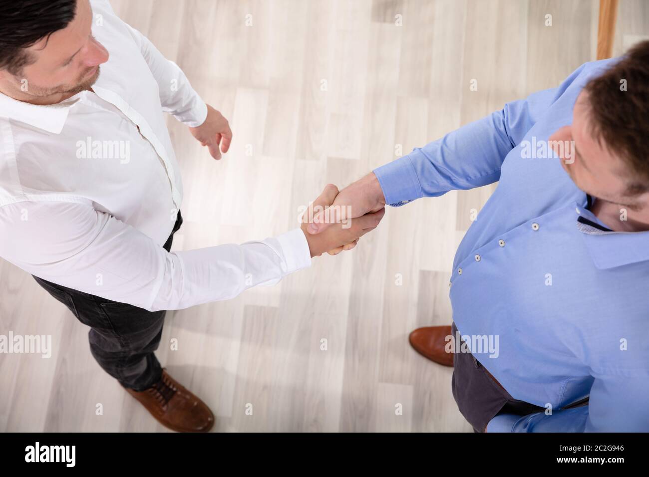 Una vista in elevazione di due imprenditori in piedi in ufficio stringono le mani Foto Stock