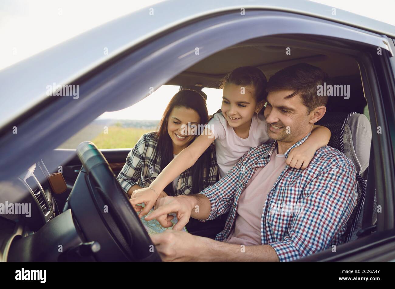 Felice giovane famiglia che cerca sulla mappa in salone di auto in viaggio. Genitori amorevoli con figlia che viaggia insieme in auto Foto Stock