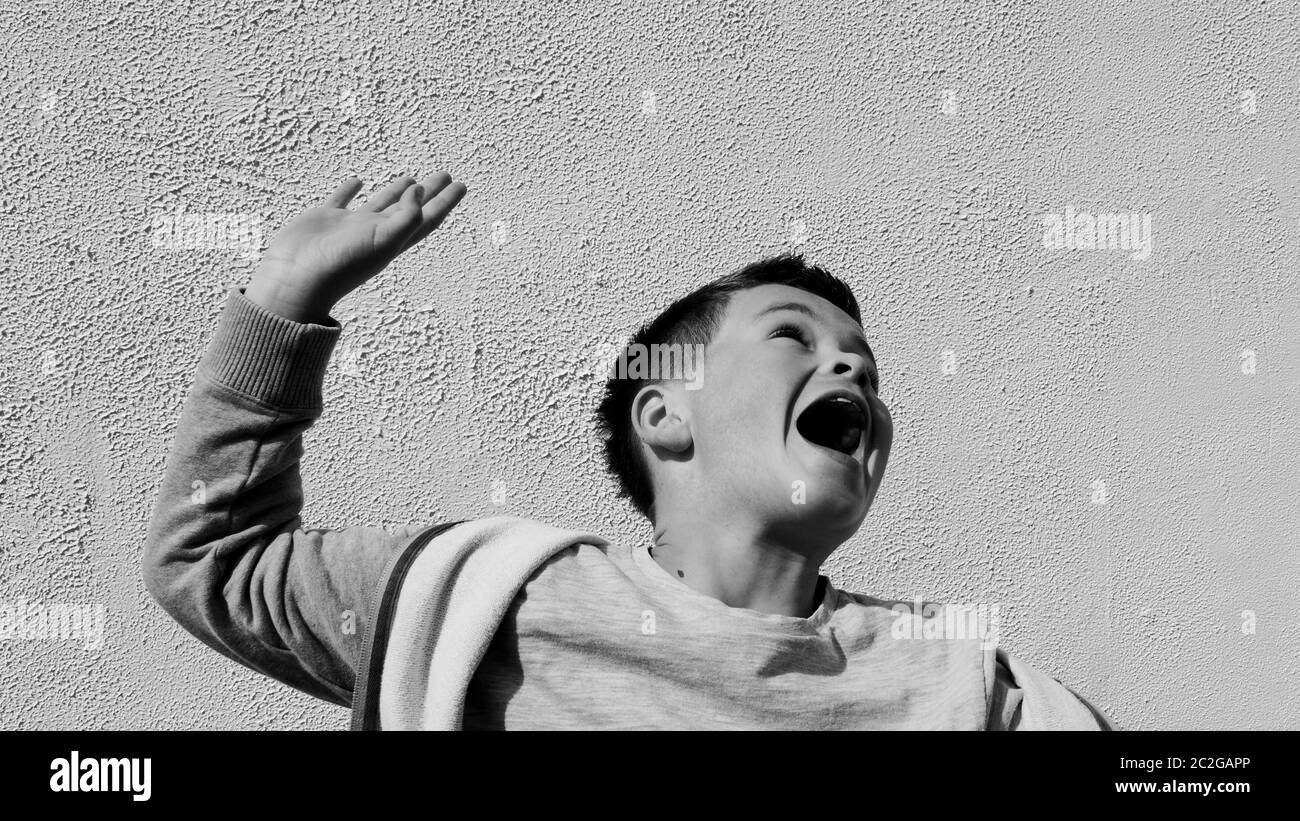 Immagine in bianco e nero - splendido ragazzo che salta per gioia contro una parete bianca testurizzata Foto Stock