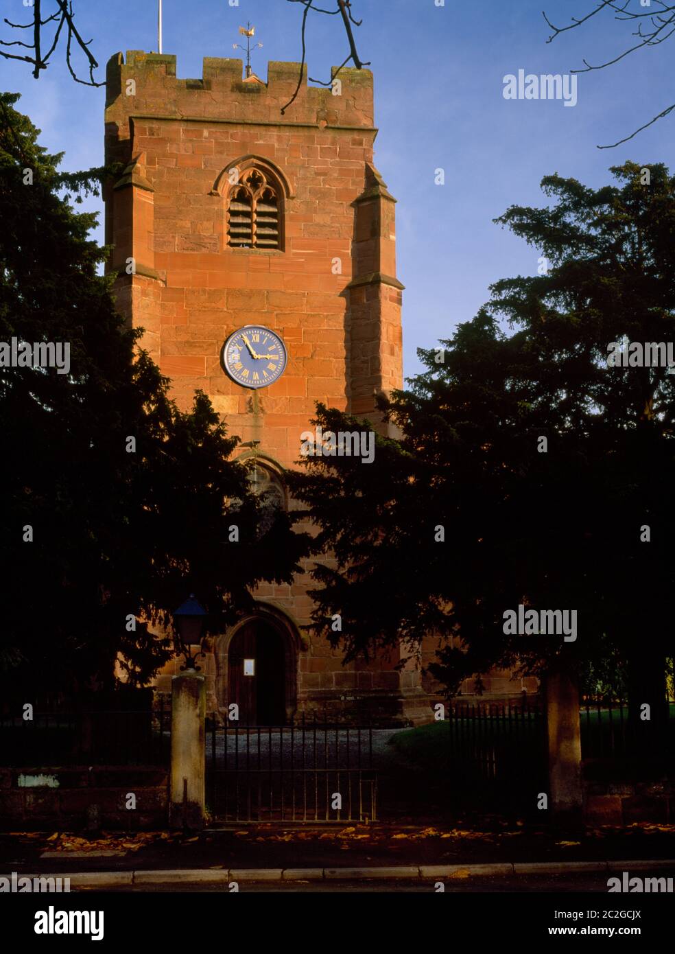 Vista e delle porte della chiesa, antichi tassi e tardo C14th W torre della chiesa di St Mary, Overton, Wrexham, Galles, Regno Unito: Orologio vittoriano di Thomas Joyce c 1849 Foto Stock