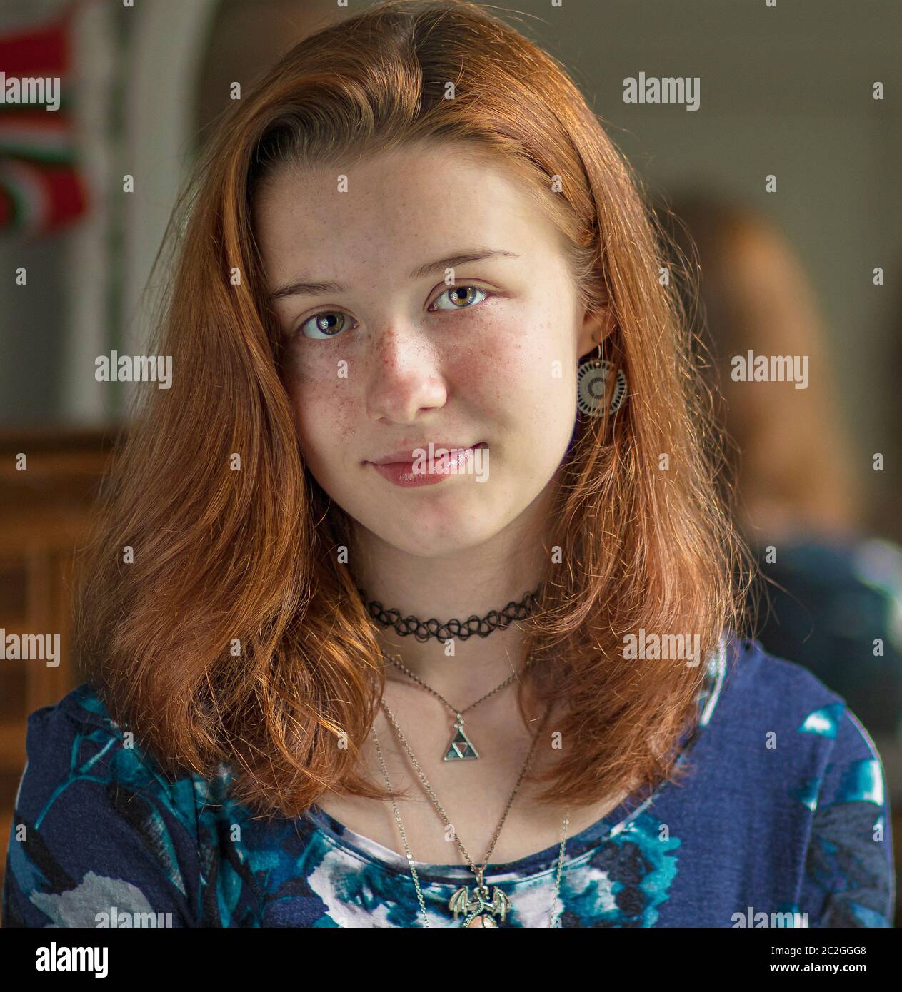 Ritratto indoor di un adolescente Pretty rosso capelli femmina con Occhi verdi blu e faccia di pale e una bocca chiusa Grin che indossa una collana choker e una blu Foto Stock