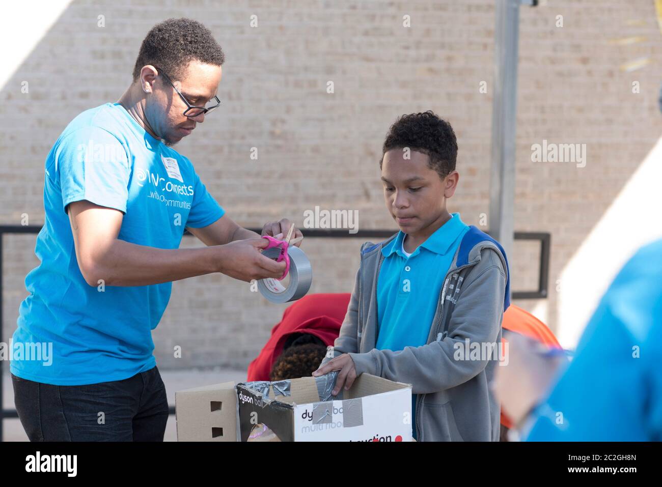 Austin Texas USA, aprile 20 2016: Un volontario adulto consiglia agli studenti della Cedars International Academy, che partecipano al programma Earth Day Cardboard Challenge della Cedars International Academy, mentre progettano e costruiscono una mostra scientifica in cartone e altri semplici prodotti riciclati. L'evento si è tenuto il giorno della Terra. ©Bob Daemmrich Foto Stock