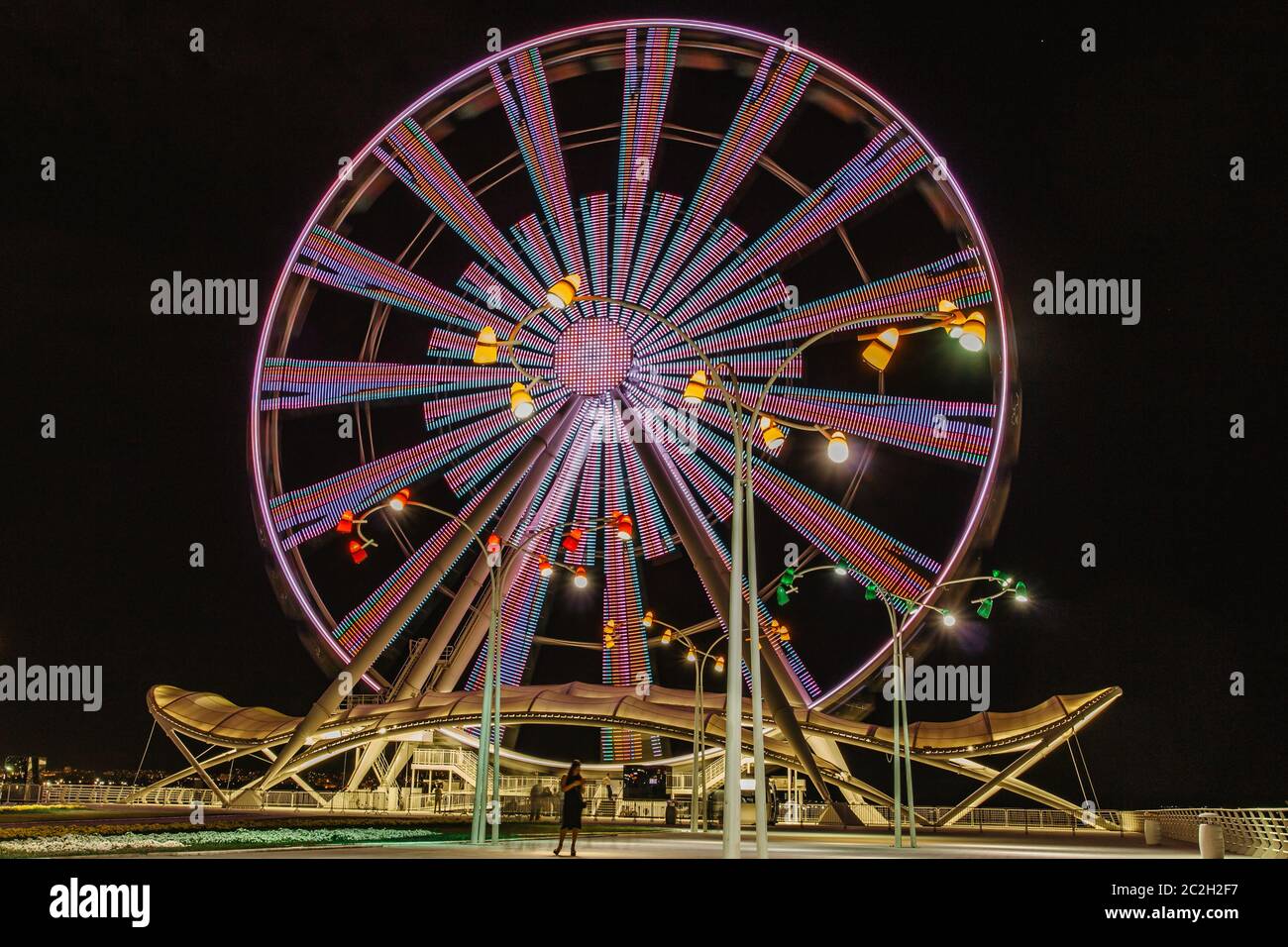 Una ruota in ferro colorata di notte. Vista frontale. Grande giostra a Baku. Divertimento notturno. Ruota panoramica su uno sfondo di cielo scuro. Ruota panoramica e rollercoa Foto Stock