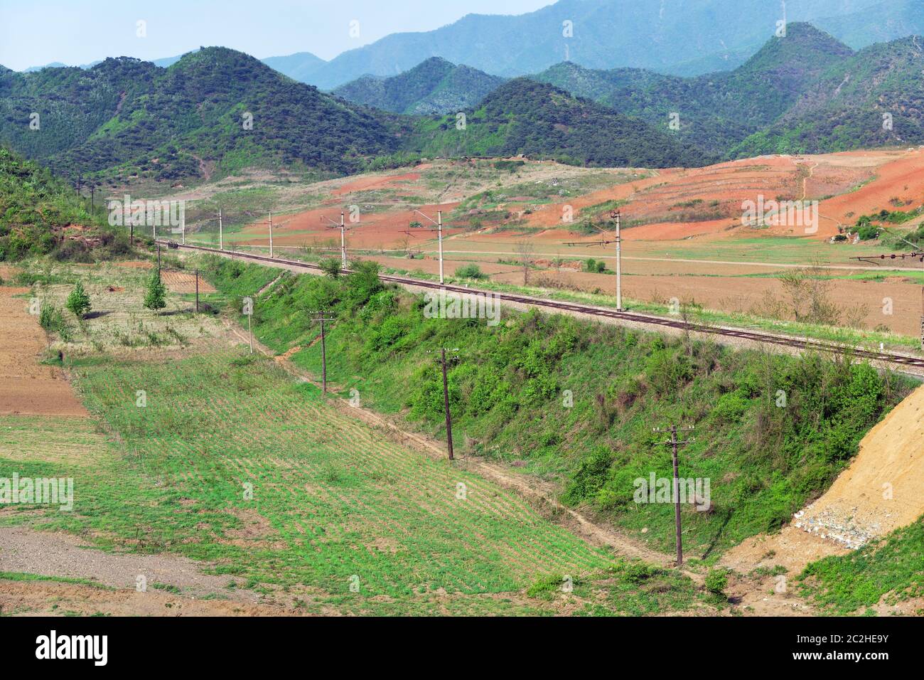 Collegamento ferroviario Corea del Nord e Corea del Sud tra i campi agricoli. Montagne sullo sfondo. Squadra di soldati che si snoda lungo la strada. Non utilizzato ora Foto Stock
