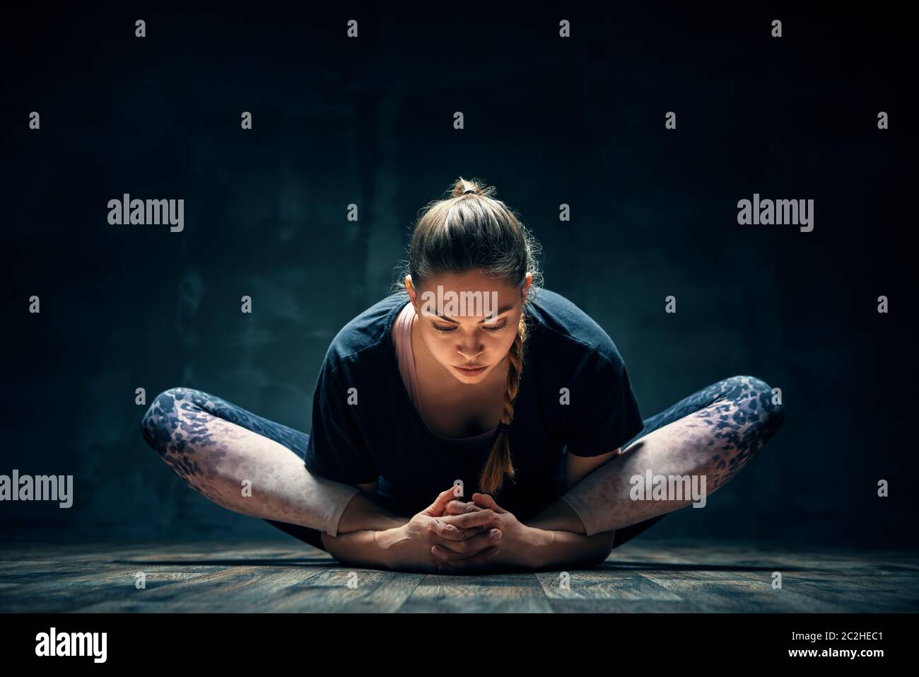Giovane donna che pratica yoga facendo la dea reclinata posa asana in camera oscura Foto Stock