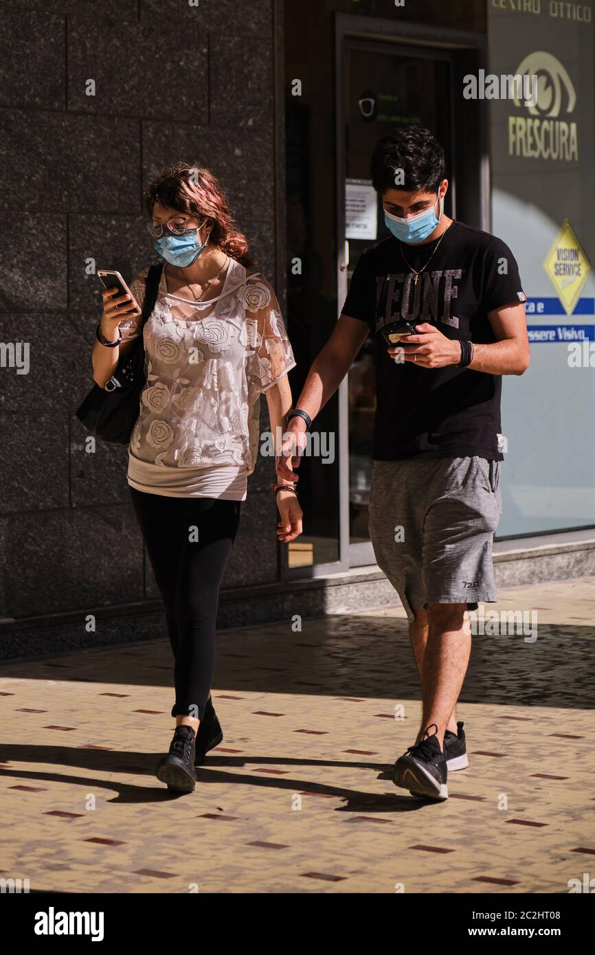 Giovane coppia smartphone protezione maschera covid-19 strada pedonale. Ragazza ragazzo sociale rapporto di distanza telefono cellulare quarantena coronavirus covid. Foto Stock