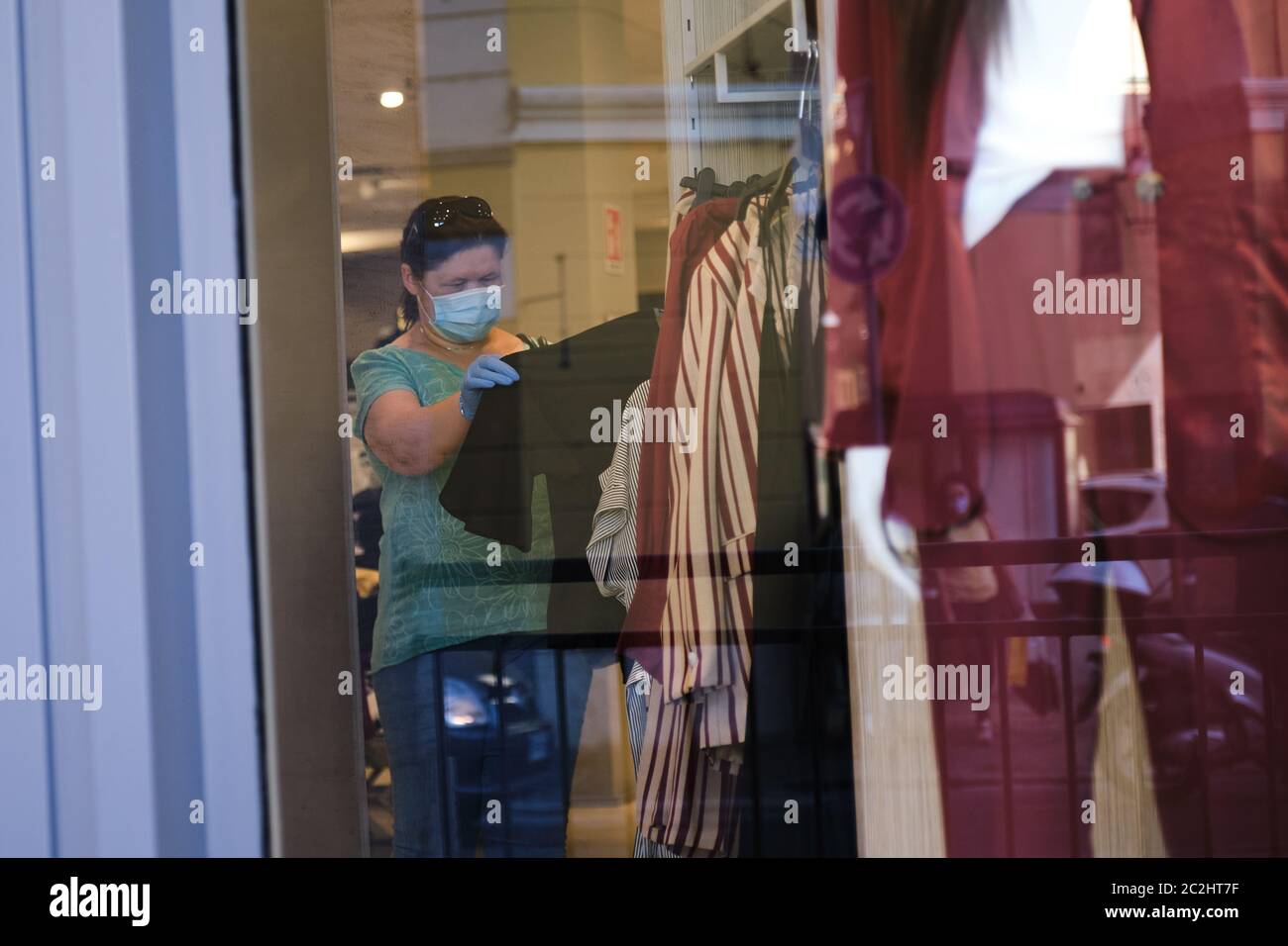 Donna shopping negozio di abbigliamento con protezione maschera covid-19 quarantena. Giovane donna che sceglie vestiti durante il coronavirus pandemico epidemico. Foto Stock