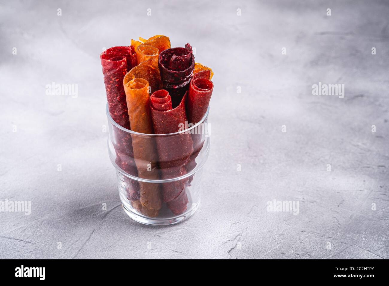 Pastiglia di frutta in tazza di vetro su fondo di pietra cemento. Alimenti biologici senza zucchero, preparati con lampone, fragola, pesca e mela. Casa vegana Foto Stock