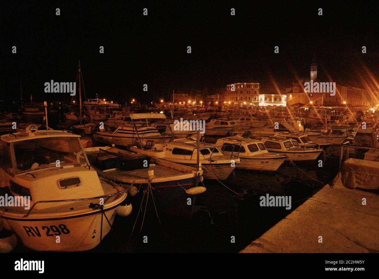 Porto di Rovigno con barche e la città con luci arancioni sullo sfondo di notte. Foto Stock