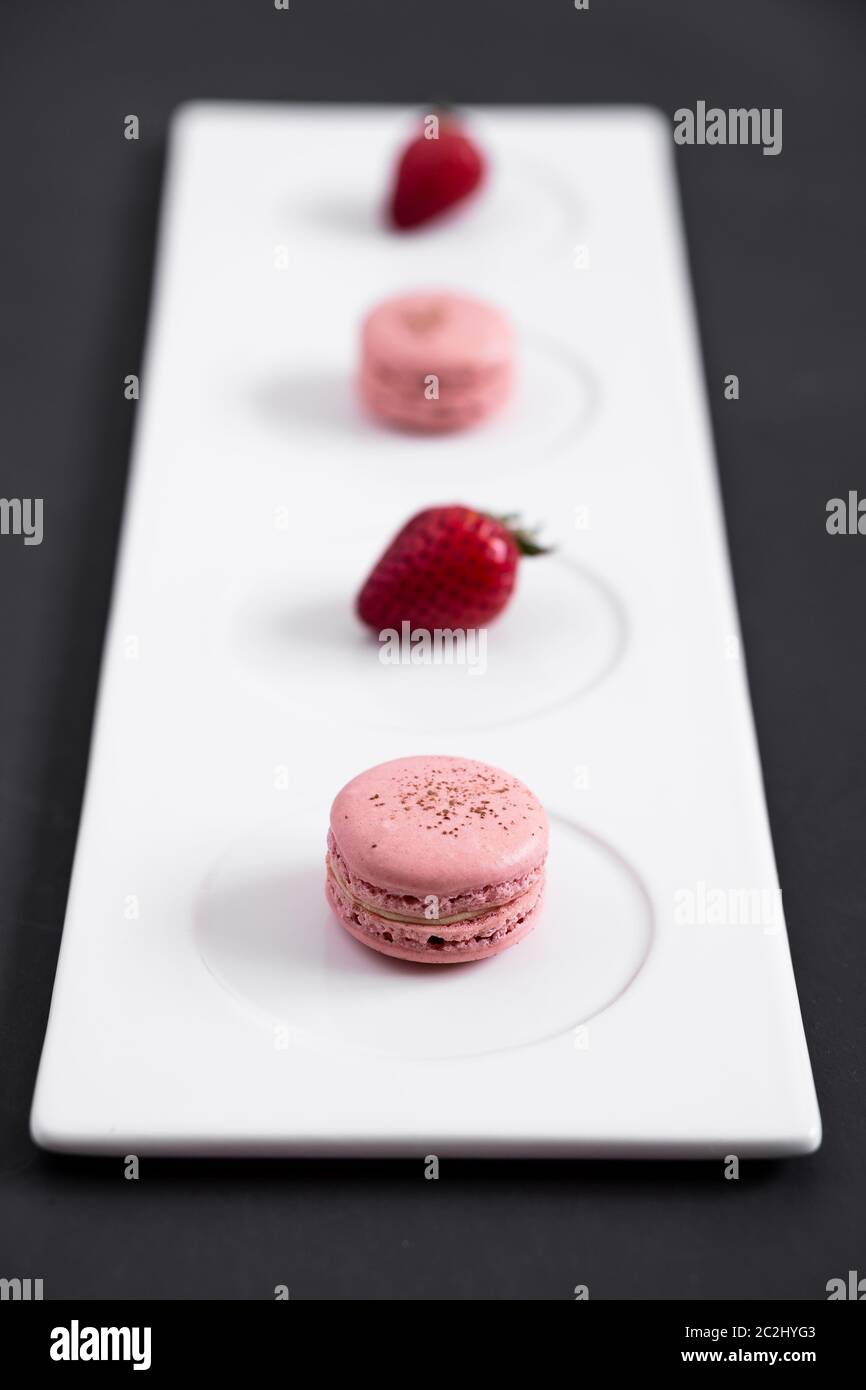 Macaron di fragole su sfondo scuro. I macaron sono delicati dolci francesi fatti di biscotti rotondi di meringa e di un ripieno dolce nel centro. Foto Stock