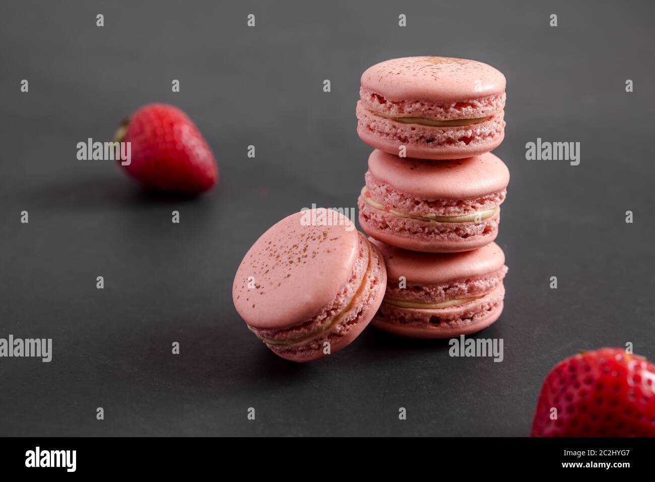 Macaron di fragole su sfondo scuro. I macaron sono delicati dolci francesi fatti di biscotti rotondi di meringa e di un ripieno dolce nel centro. Foto Stock