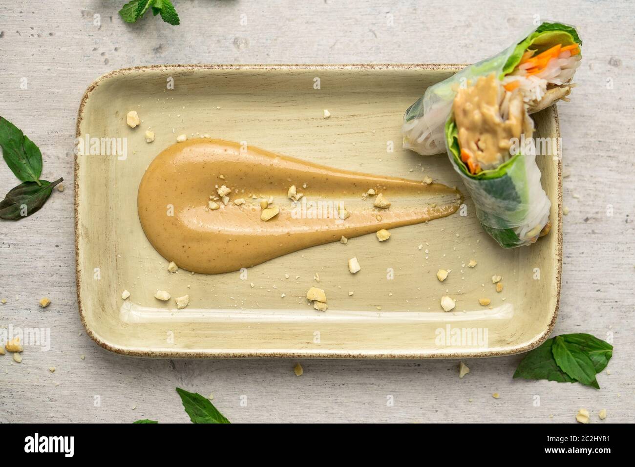Deliziosa salsa cremosa di burro di arachidi su un piatto con croccanti briciole di arachidi e involtini di primavera vietnamiti sul lato. La salsa al burro di arachidi è morbida Foto Stock