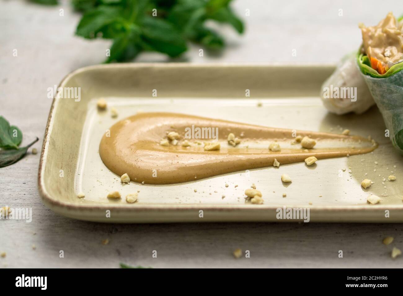 Deliziosa salsa cremosa di burro di arachidi su un piatto con croccanti briciole di arachidi e involtini di primavera vietnamiti sul lato. La salsa al burro di arachidi è morbida Foto Stock