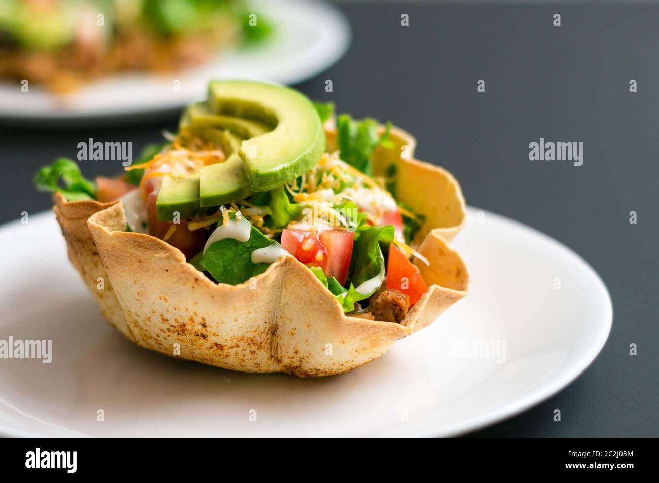 Un'insalata di taco in una ciotola di tortilla è un modo divertente e colorato di mangiare cibo messicano. Preparato con ingredienti freschi come avocado, pomodori, insalata verde, chee Foto Stock
