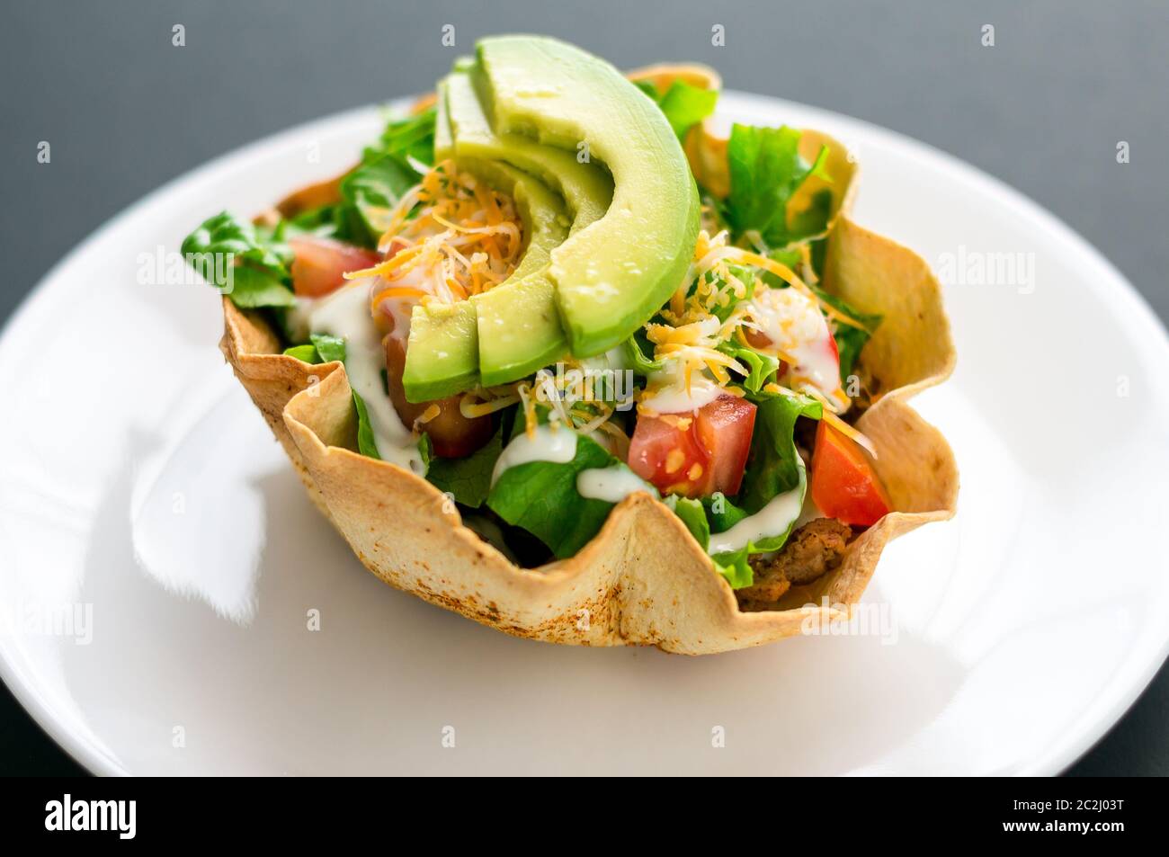 Un'insalata di taco in una ciotola di tortilla è un modo divertente e colorato di mangiare cibo messicano. Preparato con ingredienti freschi come avocado, pomodori, insalata verde, chee Foto Stock