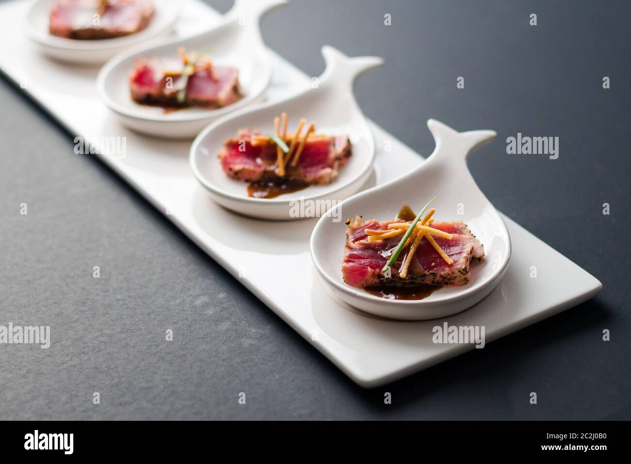 Tataki di tonno è un piatto giapponese che consiste di bistecca di tonno scottata brevemente in fette sottili. Servito come antipasto con salsa al brandy su sfondo scuro. Foto Stock