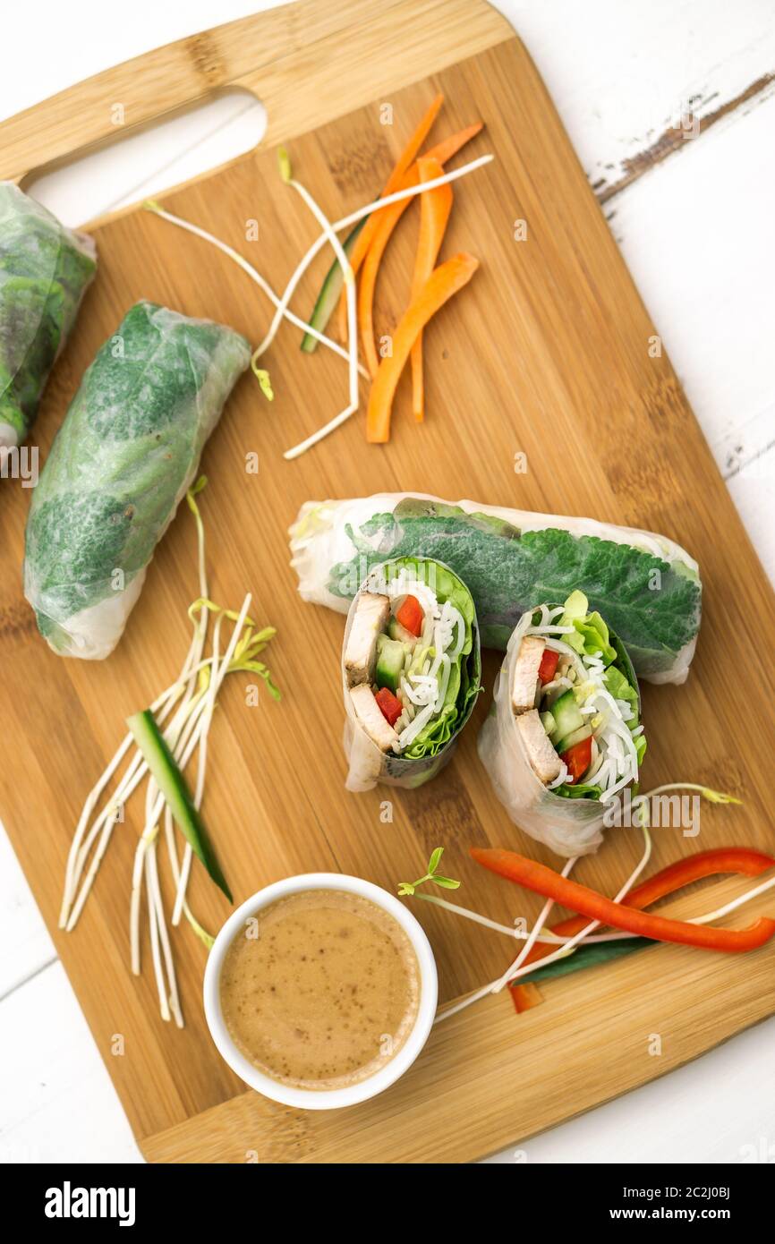 Panini freschi di primavera vietnamiti, ottimi come un antipasto sano con salsa al burro di arachidi per tuffarsi. Il cibo è posto su un tagliere di legno. Foto Stock