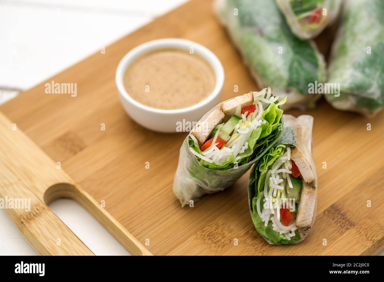 Panini estivi vietnamiti freschi, ottimi come un antipasto sano con salsa al burro di arachidi per tuffarsi. Il cibo è posto su un tagliere di legno. Foto Stock