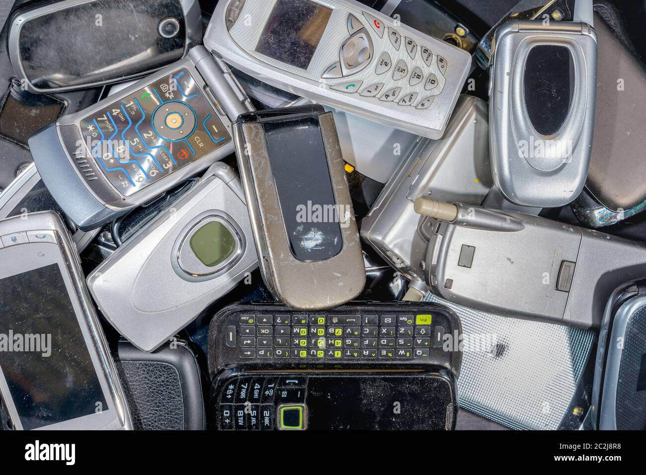 Una pila di vecchi telefoni delle cellule da riciclare. Ci sono una varietà di telefoni, ma la maggior parte sono il tipo di apertura a scatto. I telefoni sono sporchi. Il branding è stato rimosso Foto Stock
