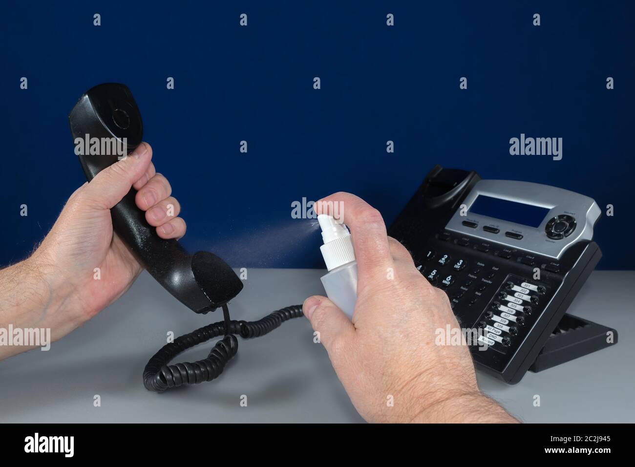 Pulire il telefono con una bottiglia di alcool spray. L'alcool viene spruzzato sul boccaglio del ricevitore. Telefono in background. Foto Stock