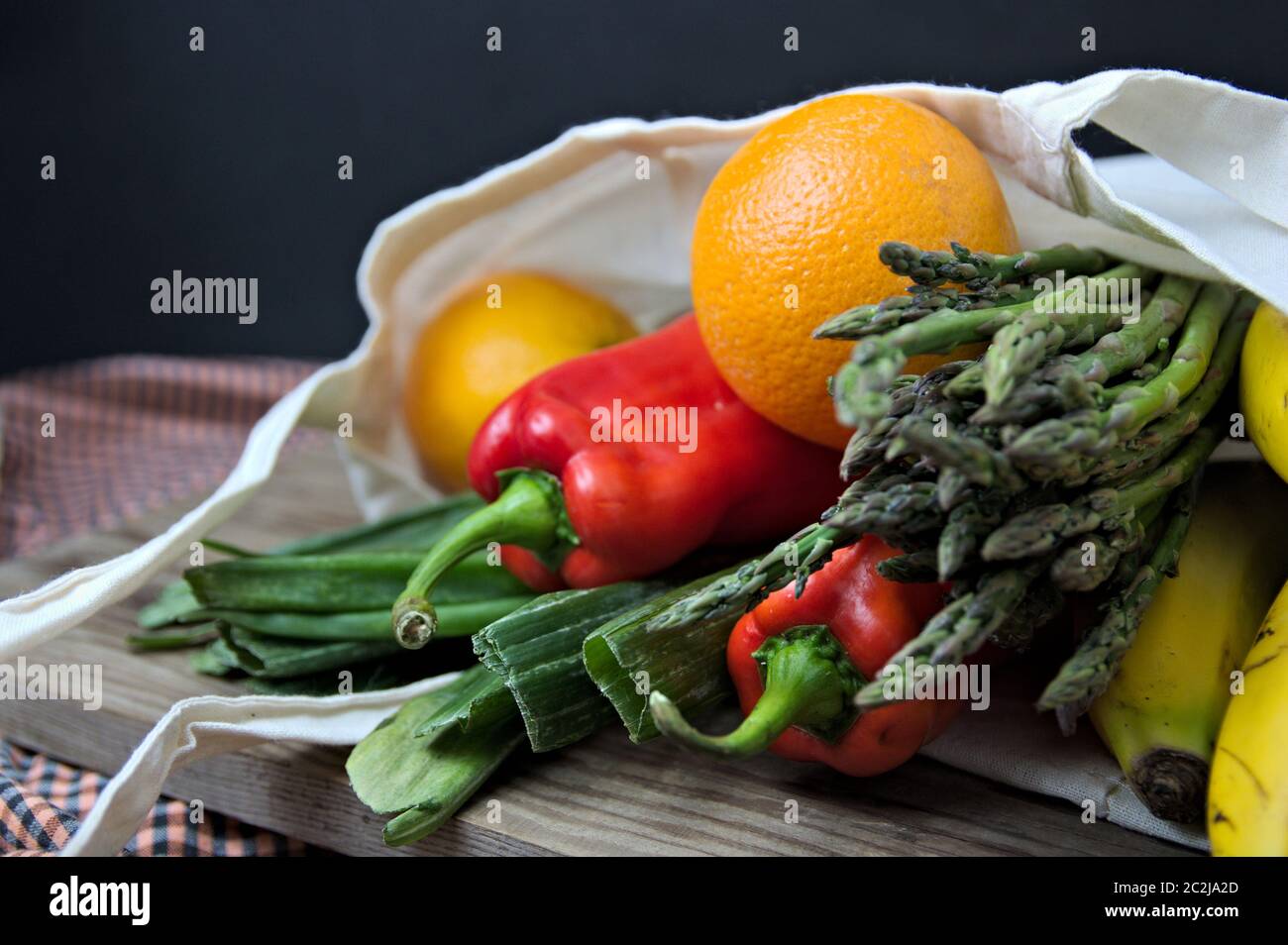 Pepi, asparagi, arance e banane su un tavolo di legno e sfondo scuro Foto Stock