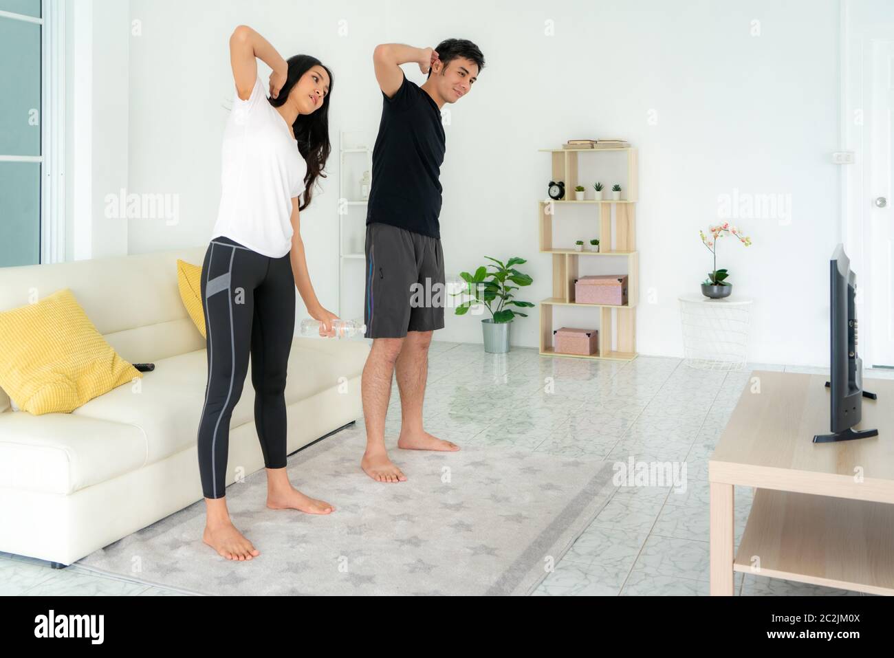 Giovane coppia asiatica che si alleva insieme ad un intervallo di alta intensità e guarda la TV a casa, uomo e donna che lavorano insieme in soggiorno, Foto Stock