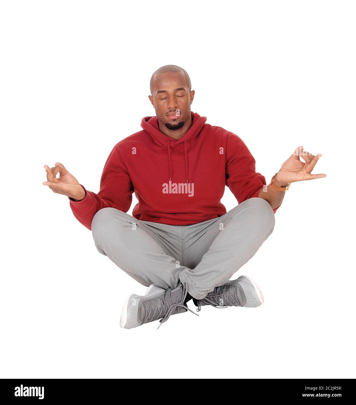 Un bel americano africano uomo seduto in una felpa con cappuccio di borgogna sul pavimento facendo il suo esercizio di yoga, isolato per sfondo bianco Foto Stock