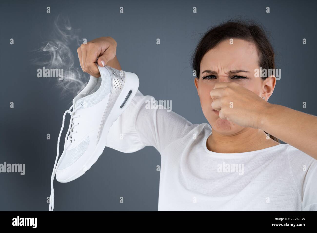 Close-up di una donna che copre il suo naso tenendo Stinky scarpe su sfondo grigio Foto Stock