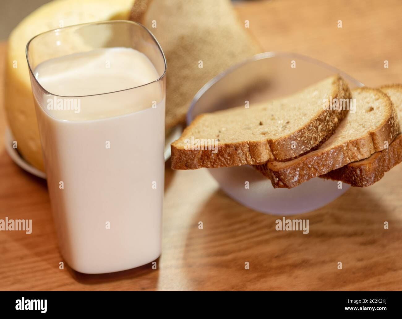 Tavolo preparato per la colazione con un bicchiere di latte, formaggio e fette di pane. Cibo umano. Prodotti da consumare accanto al caffè pomeridiano. Foto Stock