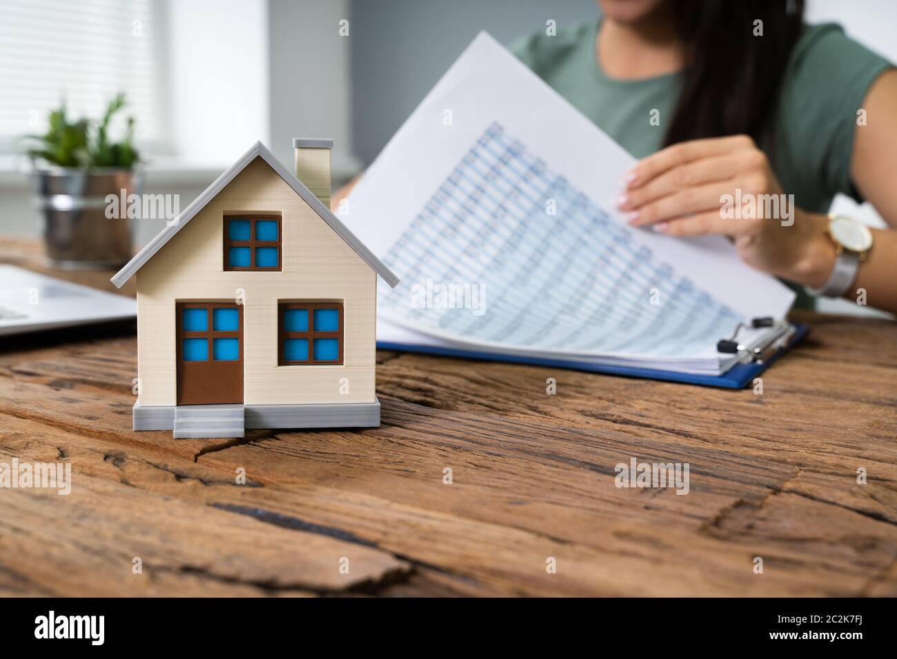 Immagine ritagliata di imprenditrice facendo il calcolo dal modello di casa sul tavolo Foto Stock