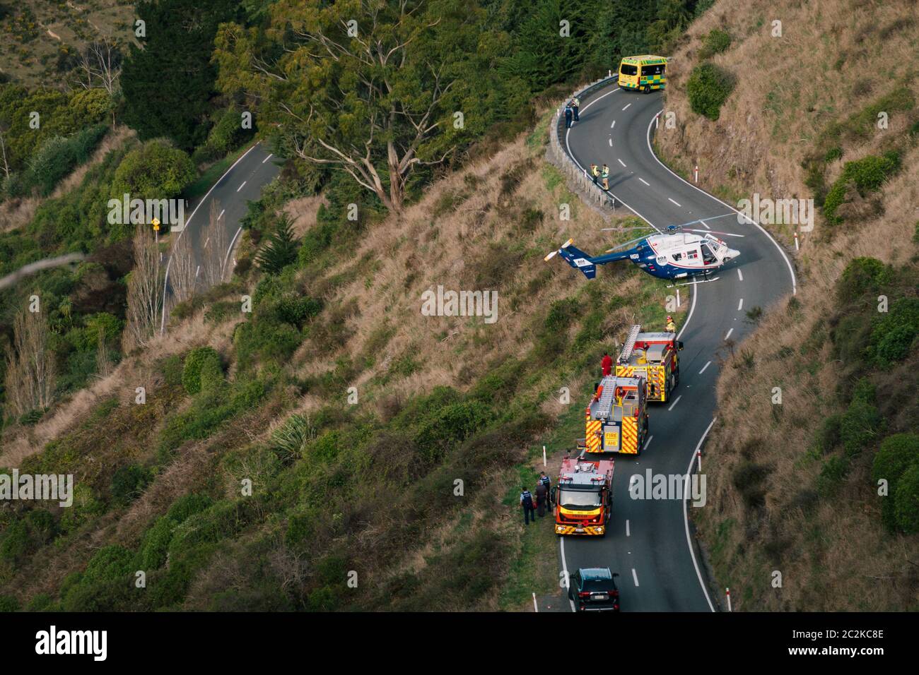 Un elicottero di soccorso è parcheggiato sulla strada, mentre i servizi di emergenza lavorano per liberare il conducente di un veicolo in discesa su una collina a Christchurch, Nuova Zelanda Foto Stock