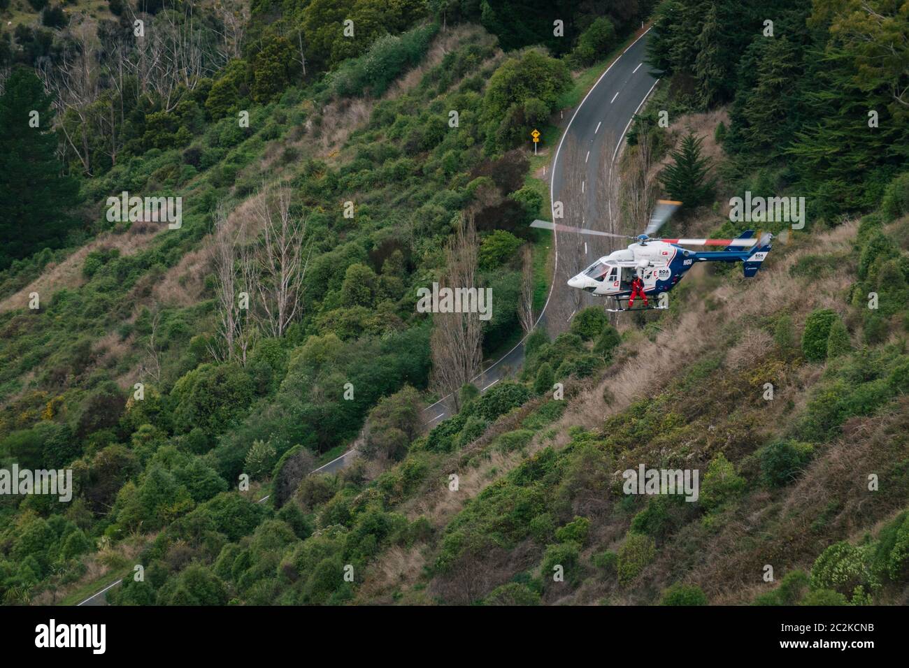 Un elicottero di salvataggio BK117 / H145 recupera il conducente di un veicolo che ha lasciato la strada e cadde su una ripida collina coperta di cespugli a Christchurch, Nuova Zelanda Foto Stock