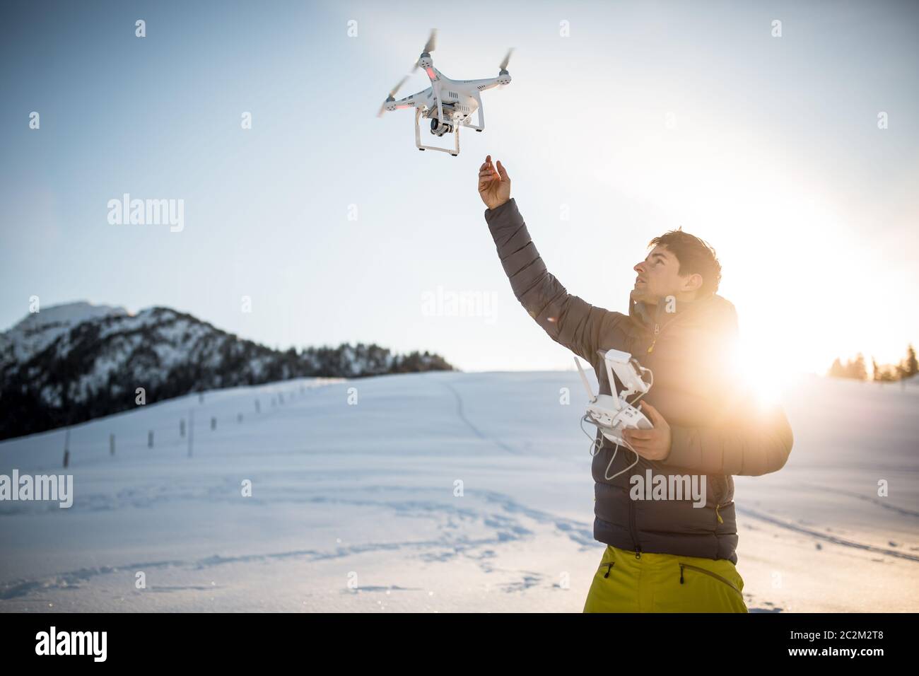 Giovane uomo che controlla il suo drone in spazi aperti innevati. Operatore drone che tiene un trasmettitore e atterra con un drone. Foto Stock