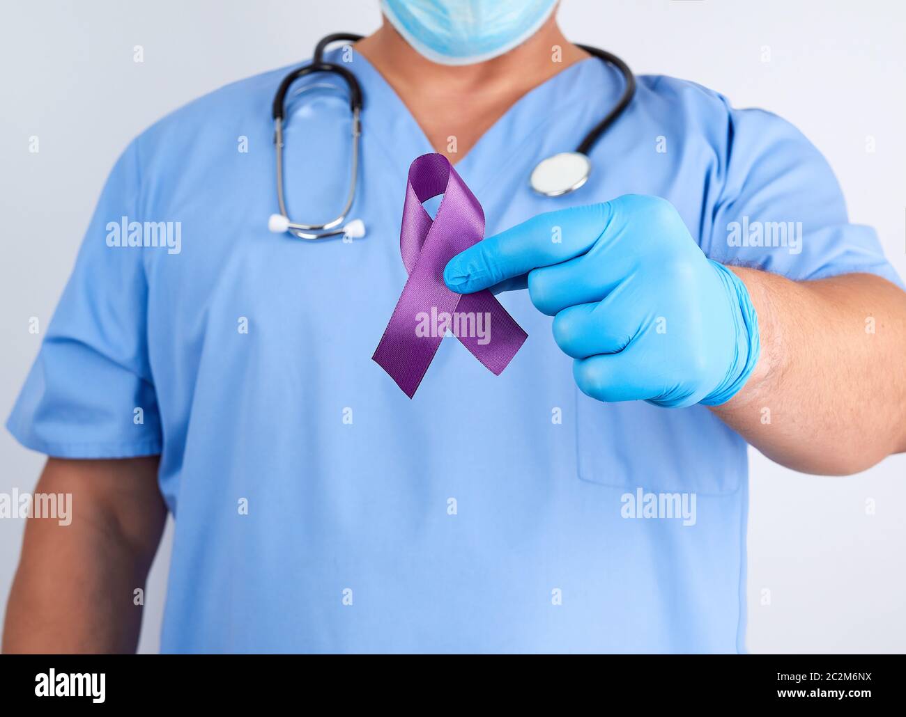 Dottore in uniforme blu e guanti in lattice contiene un nastro viola come un simbolo di inizio di ricerca e di controllo della malattia, il morbo di Alzheimer, fibrosi cistica, Foto Stock