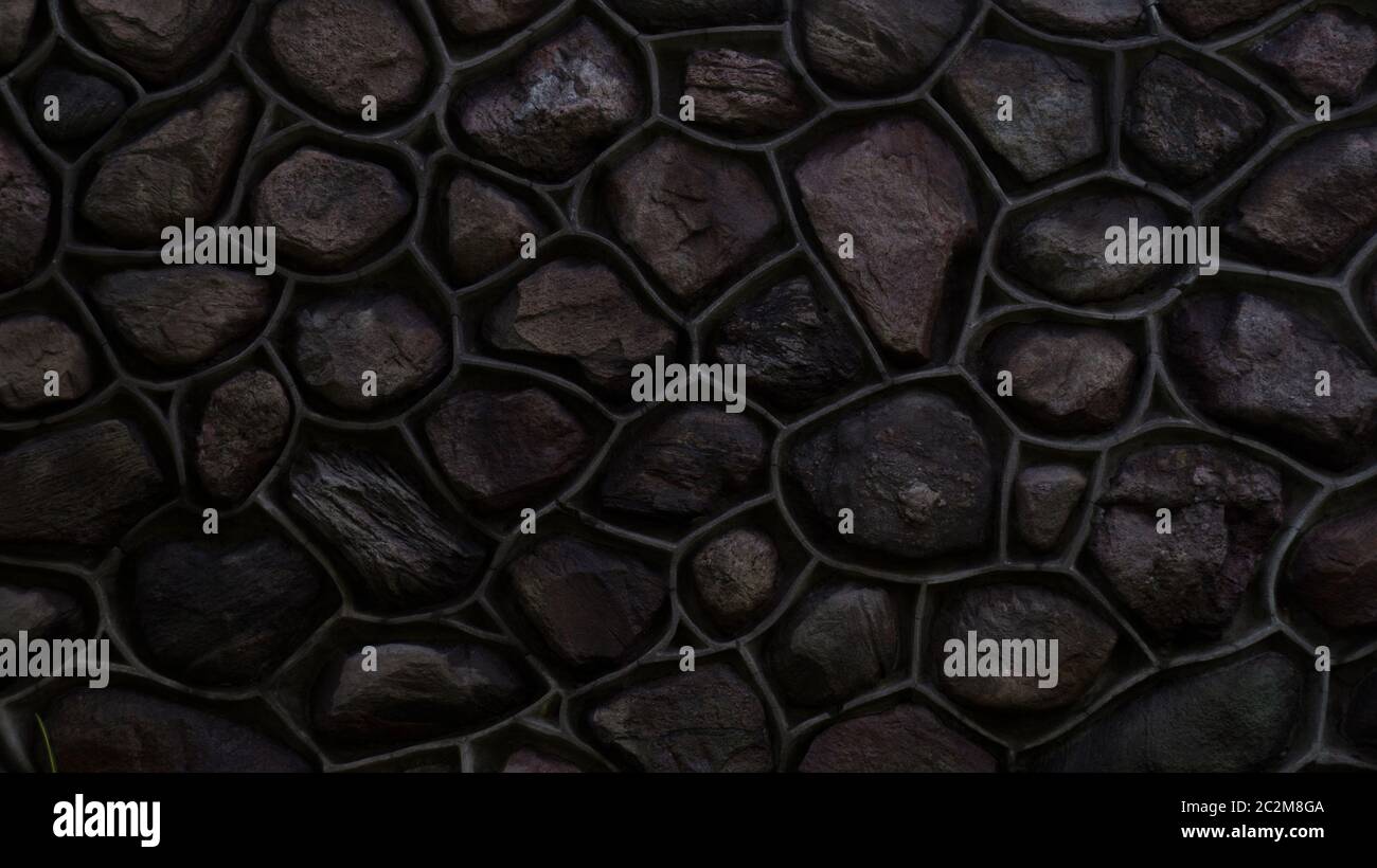 Parete scura fatta di pietra e cemento. Mosaico di rocce usate come tessere. Recinzione in pietra lucida. Struttura decorativa in materiale naturale. Sfondo, motivo Foto Stock
