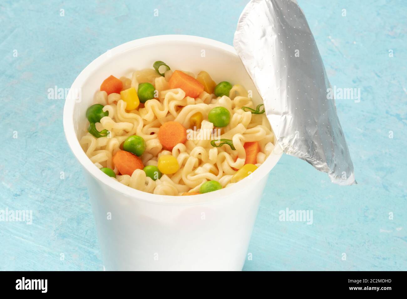 Ramen cup close-up, instant soba noodles in una tazza di plastica con verdure, su uno sfondo blu Foto Stock