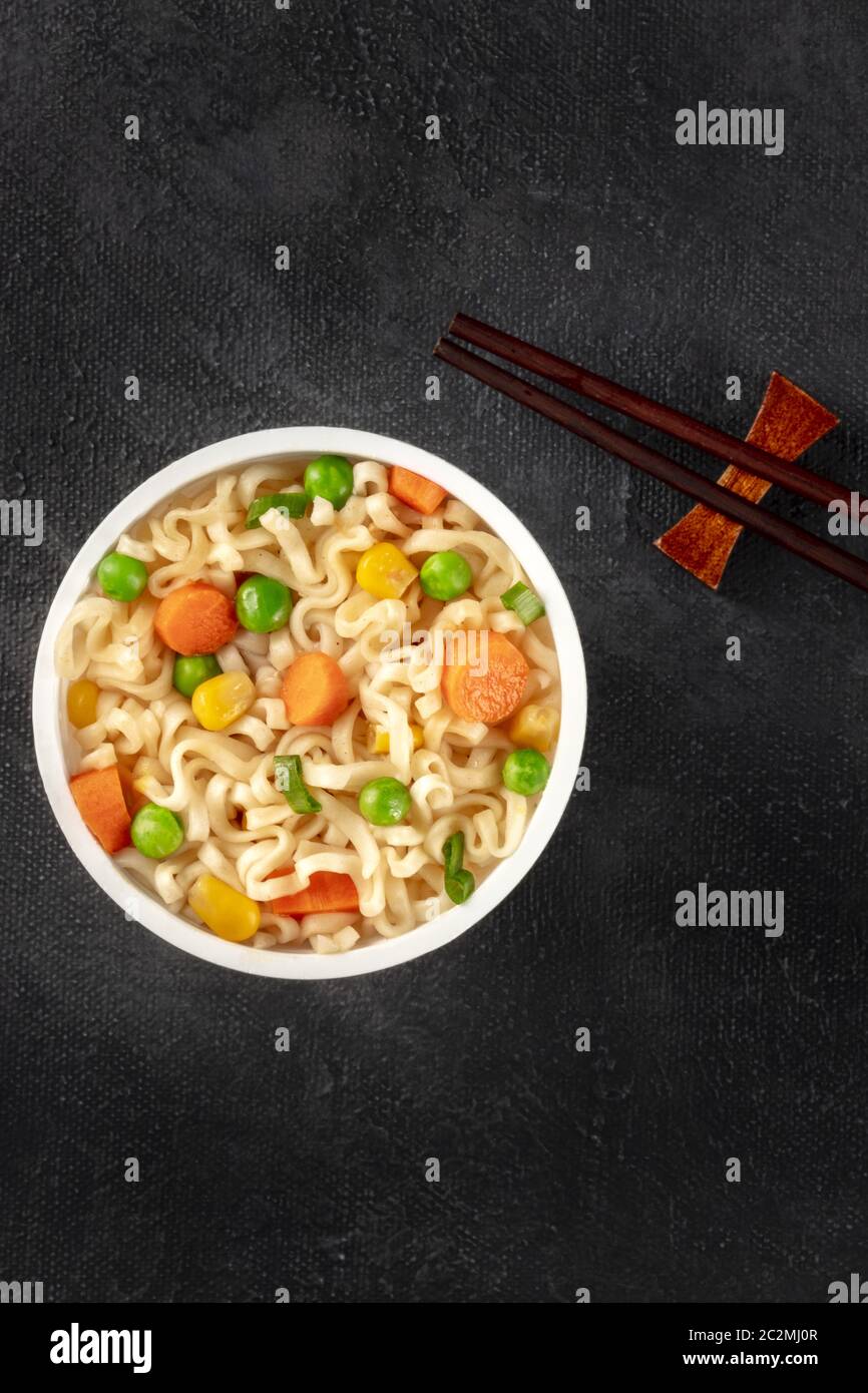 Ramen cup, tagliatelle istante in una tazza di plastica, ripresa dall'alto con bacchette e spazio copia al buio su un sfondo nero Foto Stock
