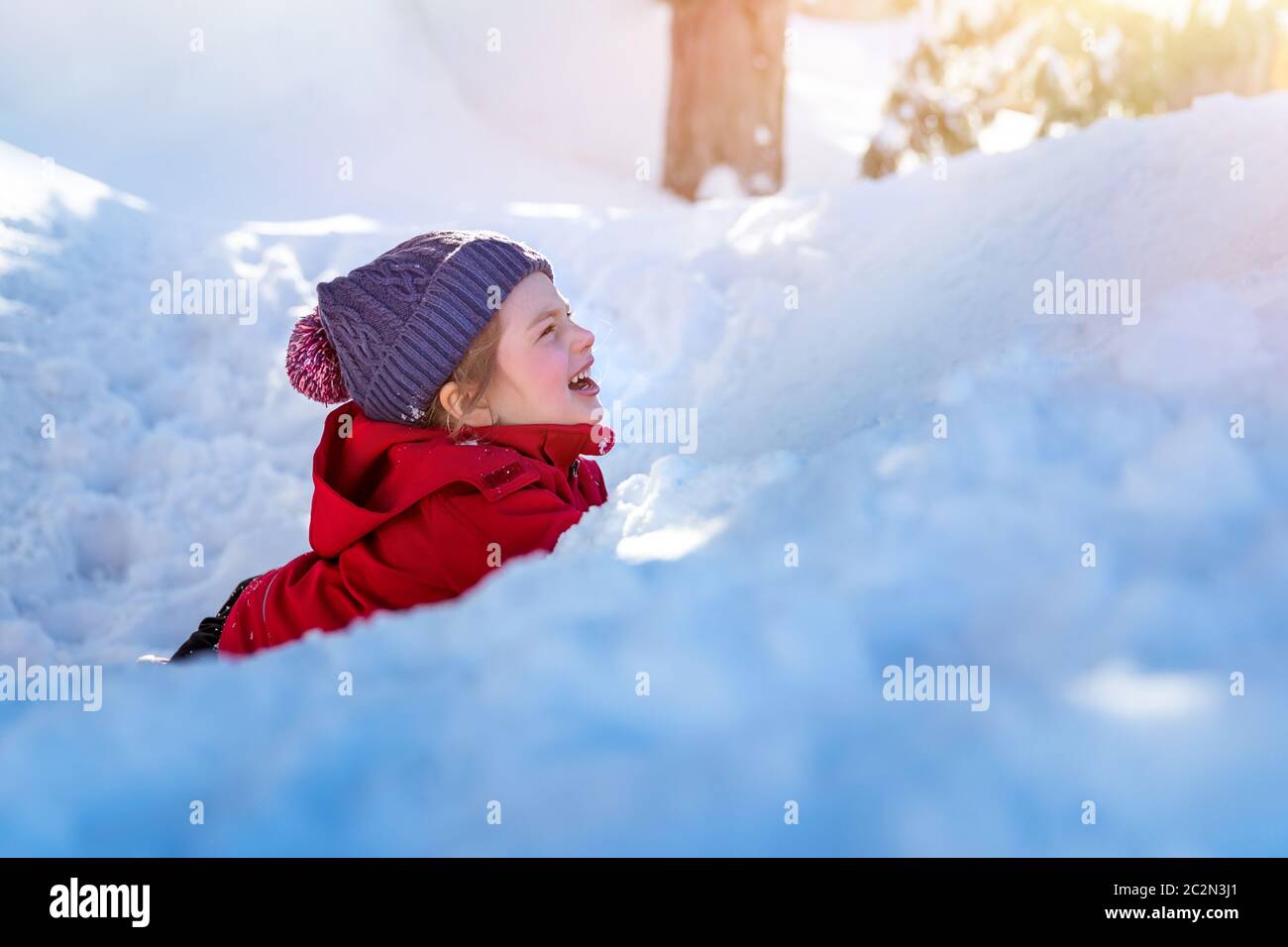 Bambino gioioso nella neve, ragazza carina allegra sdraiata nel mucchio di neve e ridendo, godendo vacanze invernali, felice infanzia spensierata Foto Stock