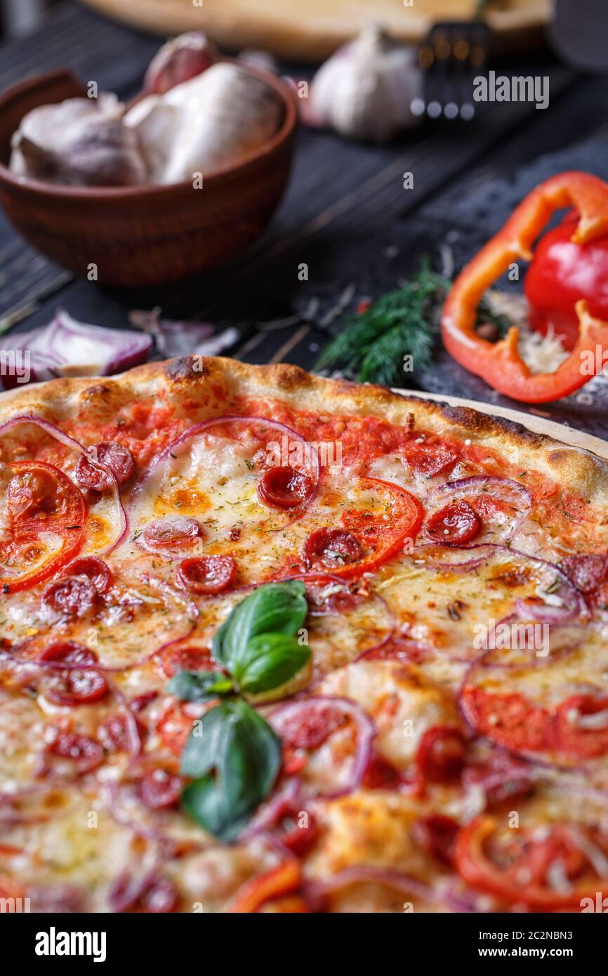 Pizza aromatica con salsicce di caccia, le cipolle e i pomodori vicino con le verdure. Sfondo pronto per il tuo design. Pizza su sfondo nero Foto Stock