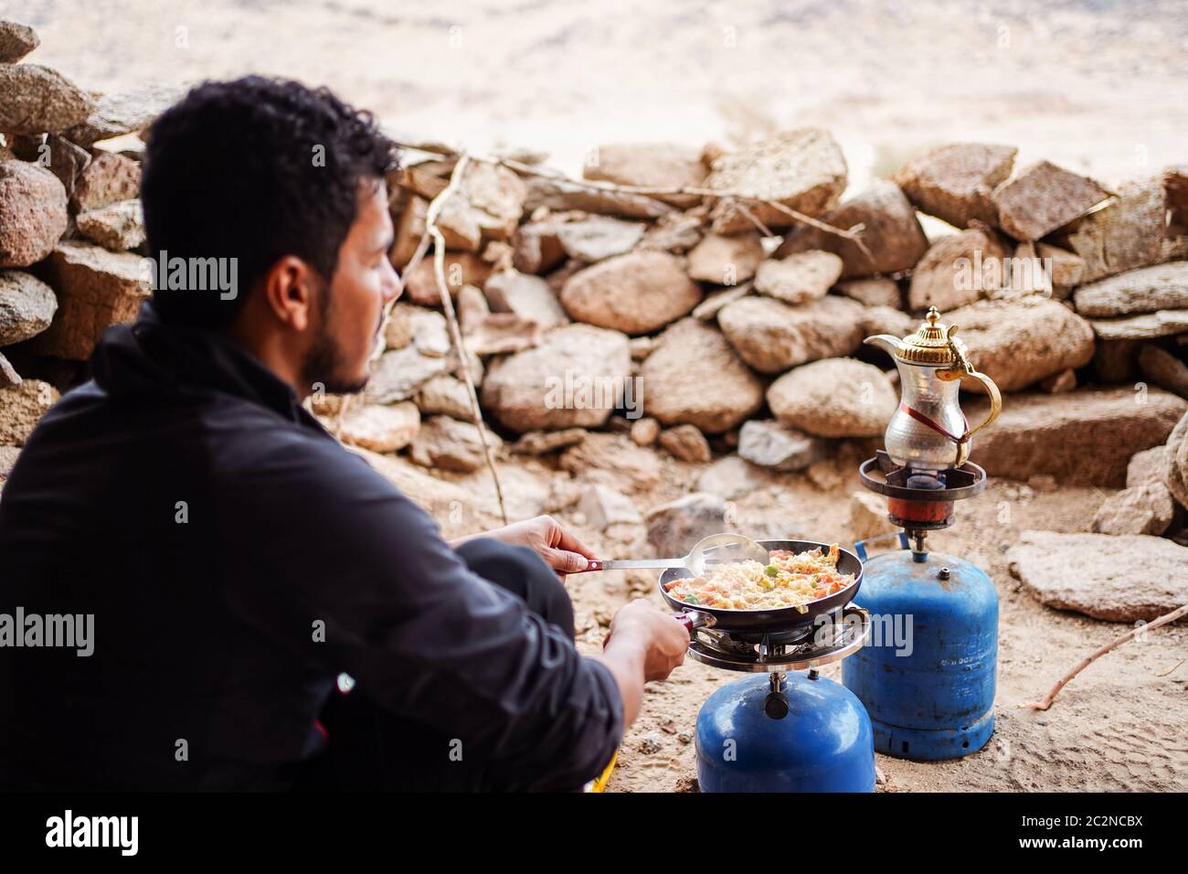 Deserto di Badr / Arabia Saudita - 20 gennaio 2020: Giovane saudita che prepara la colazione nel deserto con stufa a gas in campeggio Foto Stock