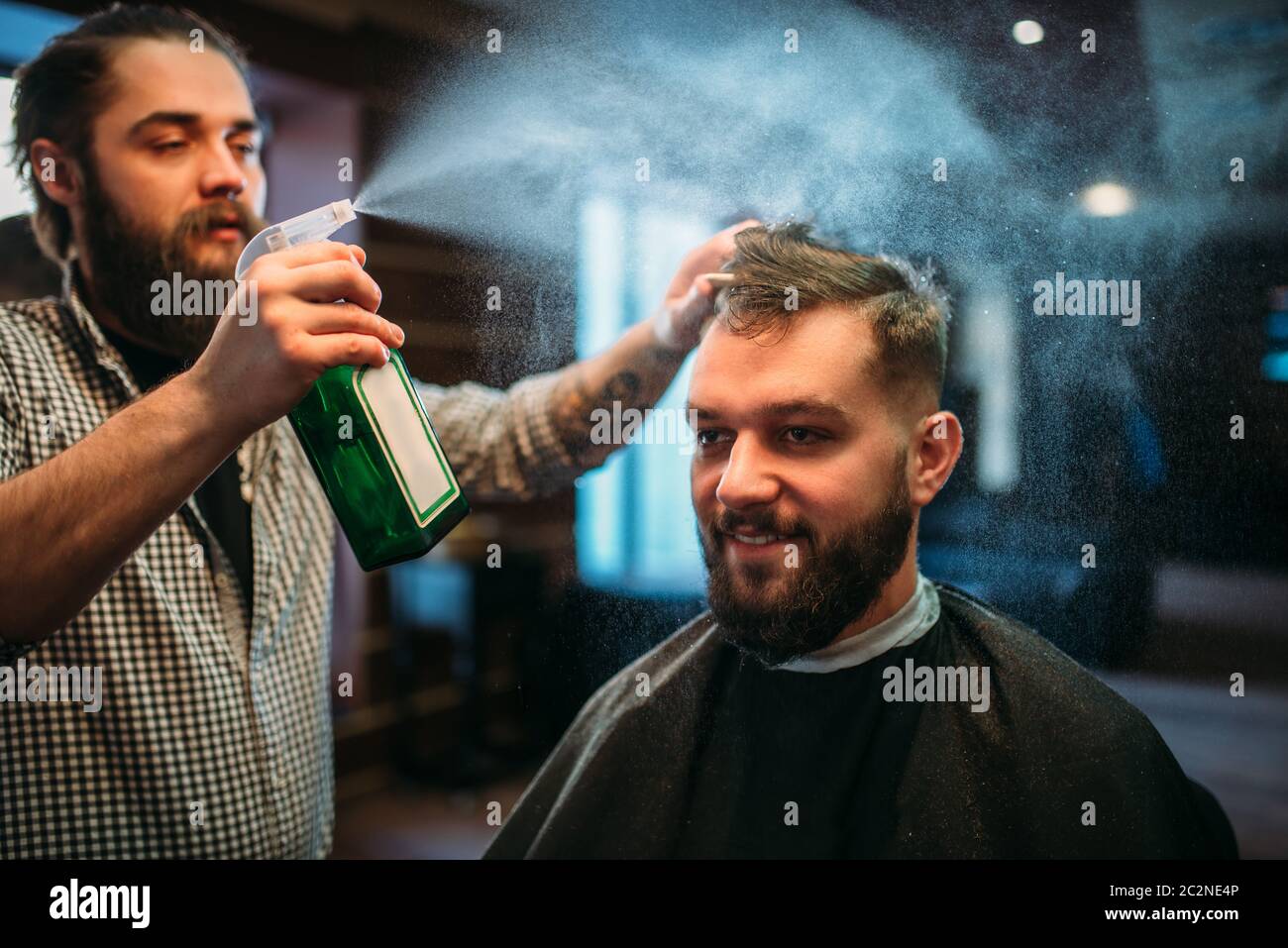 Parrucchiere acqua con spruzzo di capelli il client man in black salon cape. Persona di sesso maschile visita barbiere Foto Stock