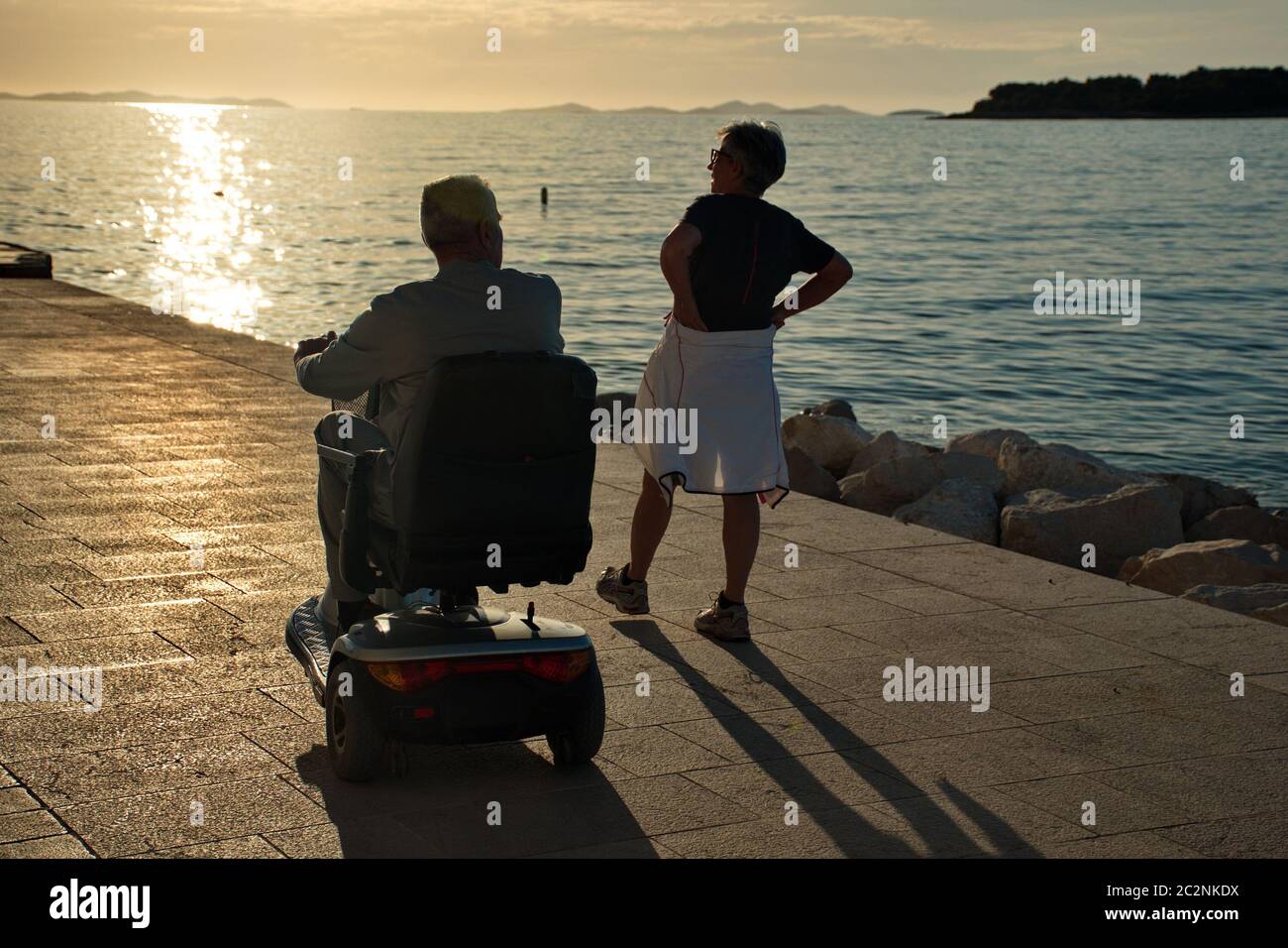 Coppia senior che cammina lungo la costa mediterranea - uomo disabile in sedia a rotelle Foto Stock