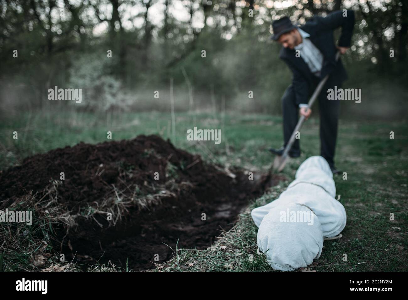 Killer sta scavando una tomba per la vittima nella foresta, il corpo avvolto in una tela, serial maniac concept Foto Stock